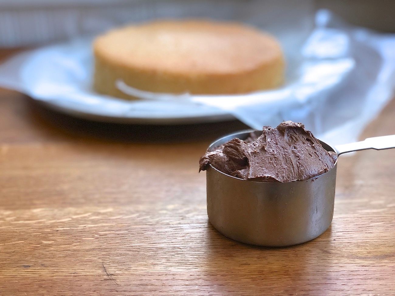 A 1-cup measure of chocolate frosting ready to be spread onto a layer cake.