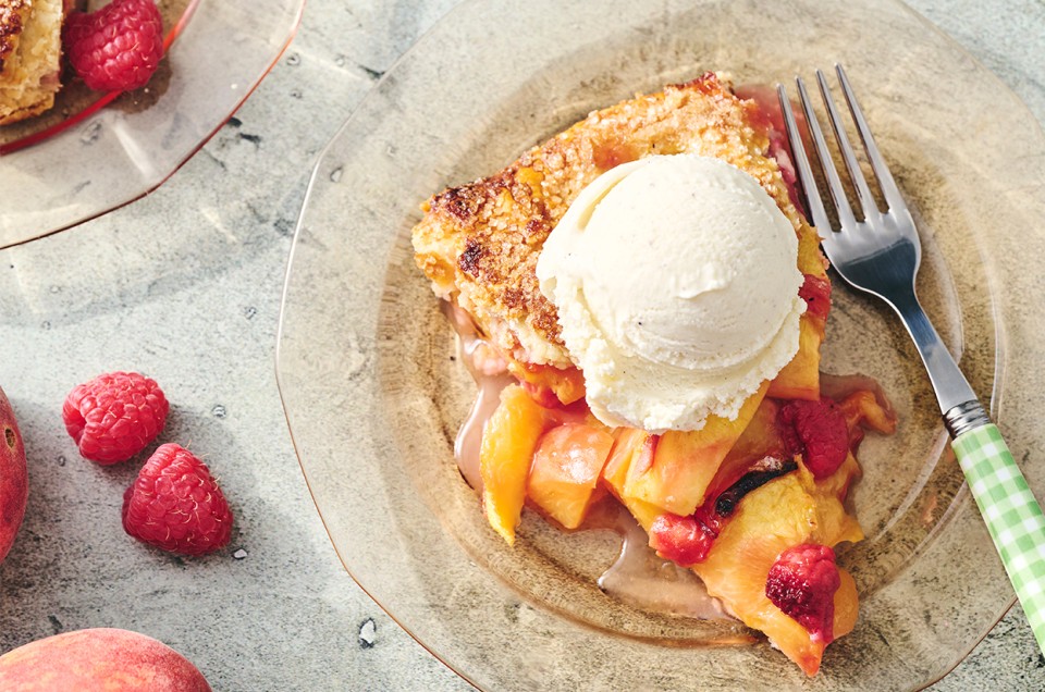 A slice of Rustic Peach Tart on a plate with a scoop of vanilla ice cream - select to zoom