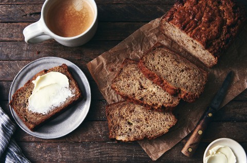 A loaf of Sourdough Banana Bread cut into slices, with one piece slathered in butter