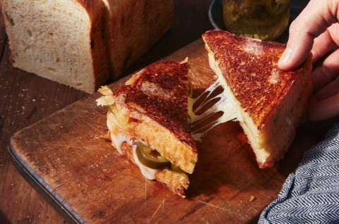 Hand pulling a triangle of a grilled cheese sandwich with cheese pull