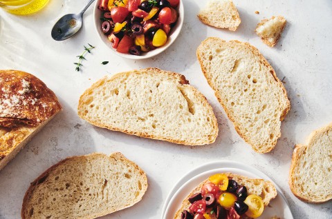 Slices of crusty bread with an even interior crumb structure, alongside a small bowl of chopped cherry tomatoes and herbs. - select to zoom