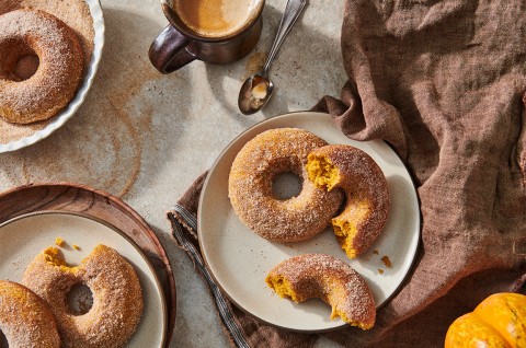 A few baked pumpkin donuts dusted in cinnamon sugar on plates, ready to be eaten. - select to zoom