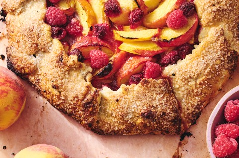 A close-up shot of a baked peach galette topped with raspberries - select to zoom
