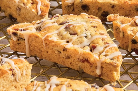 3/4 view of a fruitcake scone showing the glaze drizzled over the top and the edges with a golden brown scone dotted with fruit. - select to zoom