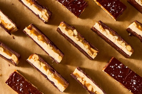 Multiple chocolate peanut nougat bars sliced and arranged on parchment paper showing the layers of chocolate, nougat, caramel, and peanuts. - select to zoom