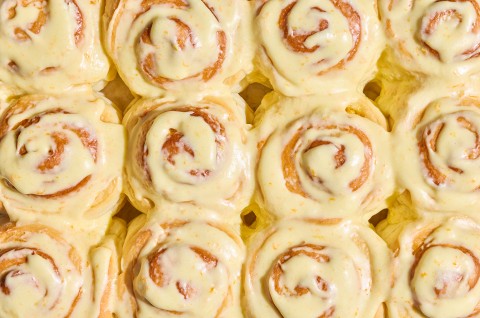 Detail shot of several Fluffy Frosted Orange Rolls together seen from above with a glossy yellow citrus glaze. - select to zoom