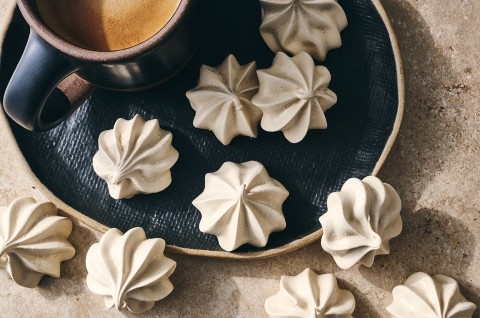 Espresso Meringues photographed from above and randomly spread on a dark plate with a cup of coffee in the upper left of the image. - select to zoom