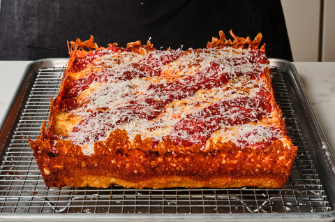 Detroit pizza on a baking rack showing the cooked pizza edges with crispy cheese and dough and a thick overall pizza. - select to zoom