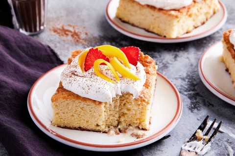 A slice of Tres Leches Cake topped with whipped cream on a plate