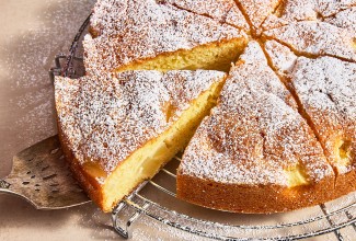 A slice being removed from a Pear and Almond Cake on a cooling rack