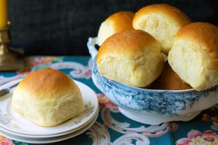 Golden soft dinner rolls in a bowl, one on a bread plate.