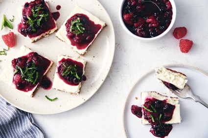 Two plates of keto-friendly cheesecake bars topped with fruit sauce