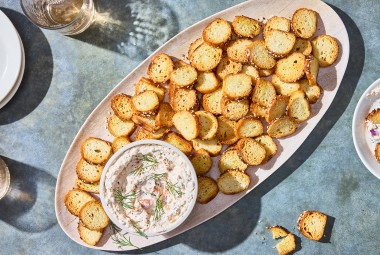 A platter of Everything Bagel Chips spread out around a small bowl of Smoked Salmon Cream Cheese dip.