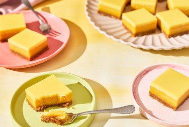 A table set with pastel colored tableware and plates with Passionfruit Bars spread out.