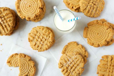 An assortment of Classic Peanut Butter Cookies on a kitchen table next to a glass of milk with a straw